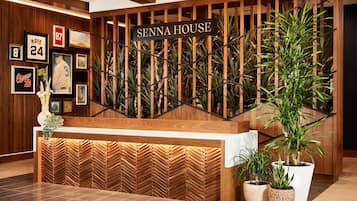 Un área de recepción con un mostrador de madera, un cartel que dice "SENNA HOUSE" y varios recuerdos deportivos en la pared.
