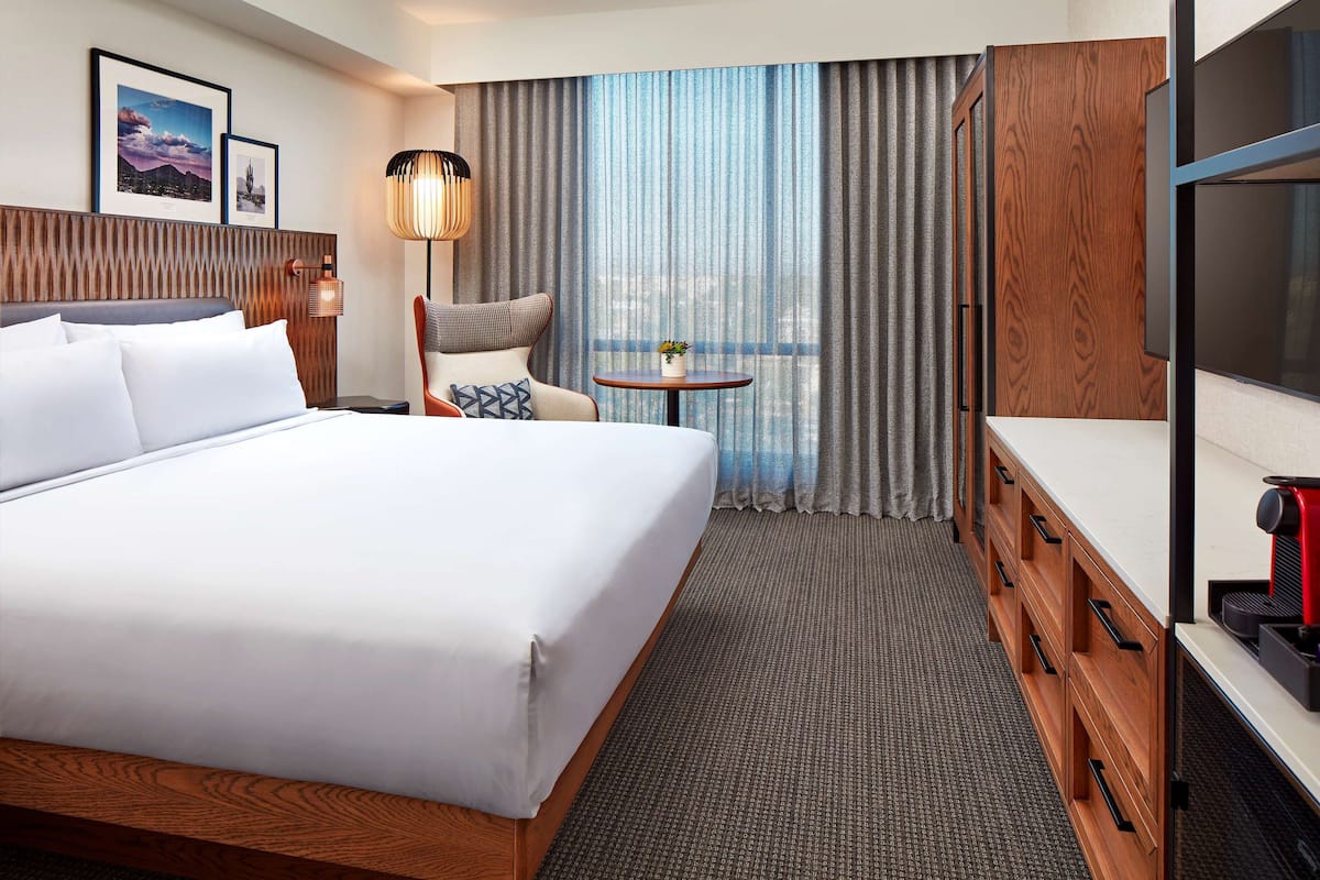 Ein Hotelzimmer mit einem großen Bett, einem Schreibtisch mit Kaffeemaschine, einem Sessel, einem kleinen Tisch und einem Fernseher.