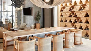 A modern interior with a long wooden table, wicker chairs, a TV, and a wine rack.