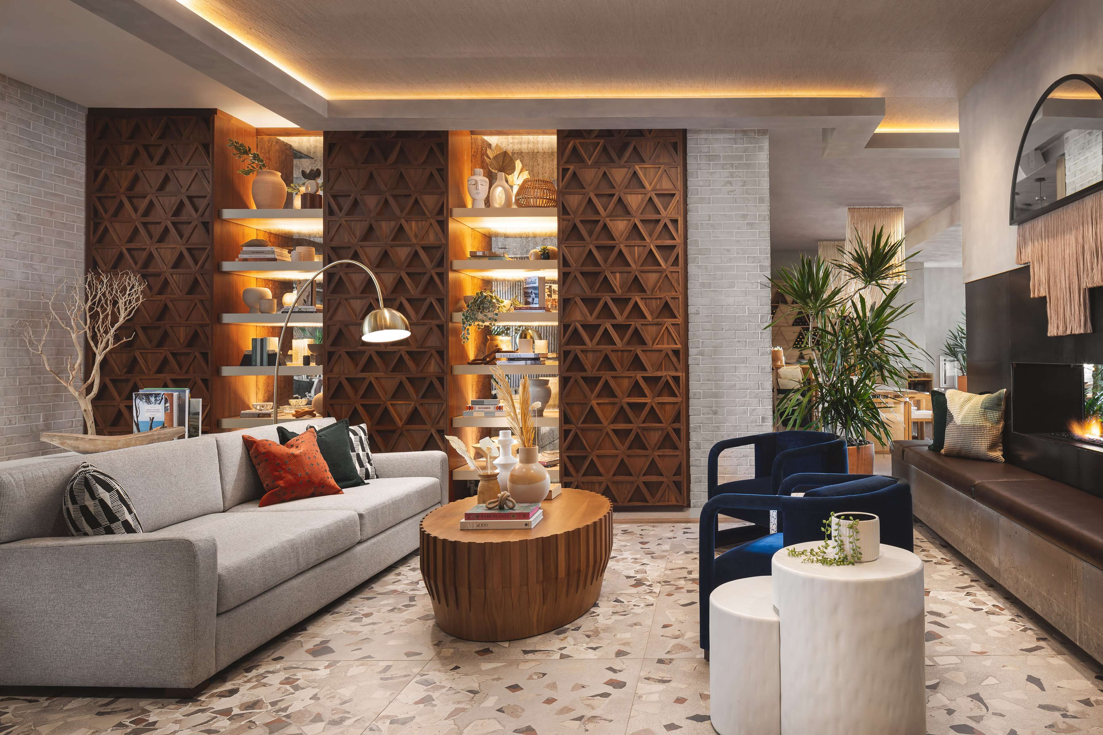 A modern living room with a sofa, coffee table, and chairs, featuring a brick wall, wooden shelving, and a fireplace.