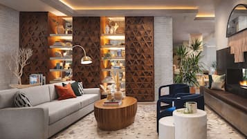 A modern living room with a sofa, coffee table, and chairs, featuring a brick wall, wooden shelving, and a fireplace.