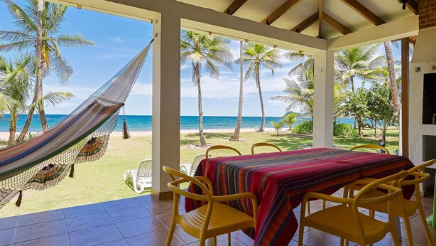 A covered outdoor dining area with a view of the beach and palm trees.