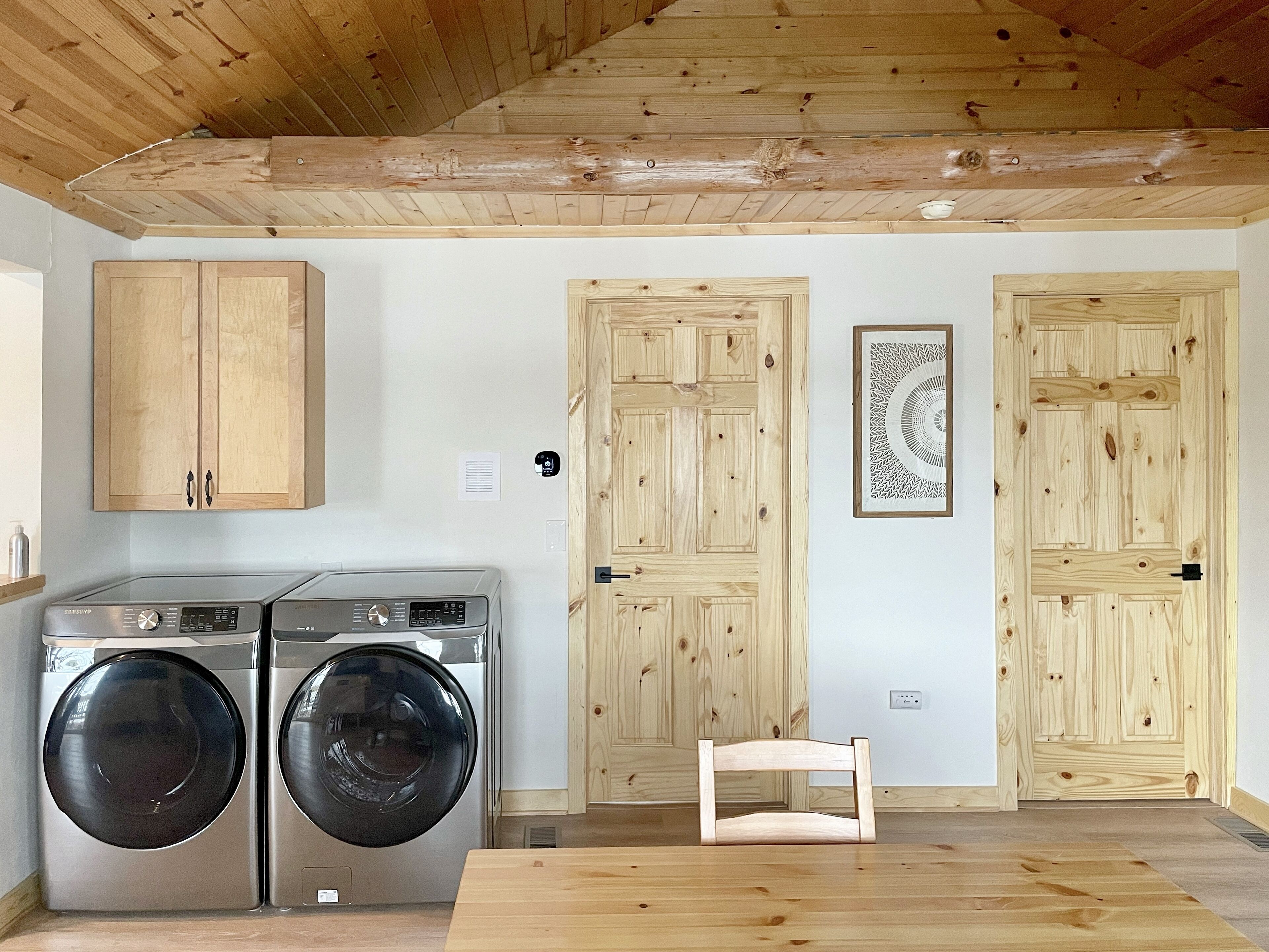 A laundry room with two washing machines, wooden cabinets, and a chair.
