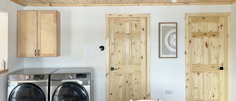 A laundry room with two washing machines, wooden cabinets, and a chair.