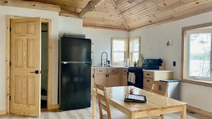 A kitchen with wooden cabinets, a black refrigerator, a dining table with chairs, and a window with a view of trees. - The BL Cottage - Lake Getaway with Panoramic Views, near Cascade Mountain (Montello)
