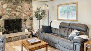 A cozy living room with a stone fireplace, a leather sofa, and a wooden coffee table. - The BL Cottage - Lake Getaway with Panoramic Views, near Cascade Mountain (Montello)