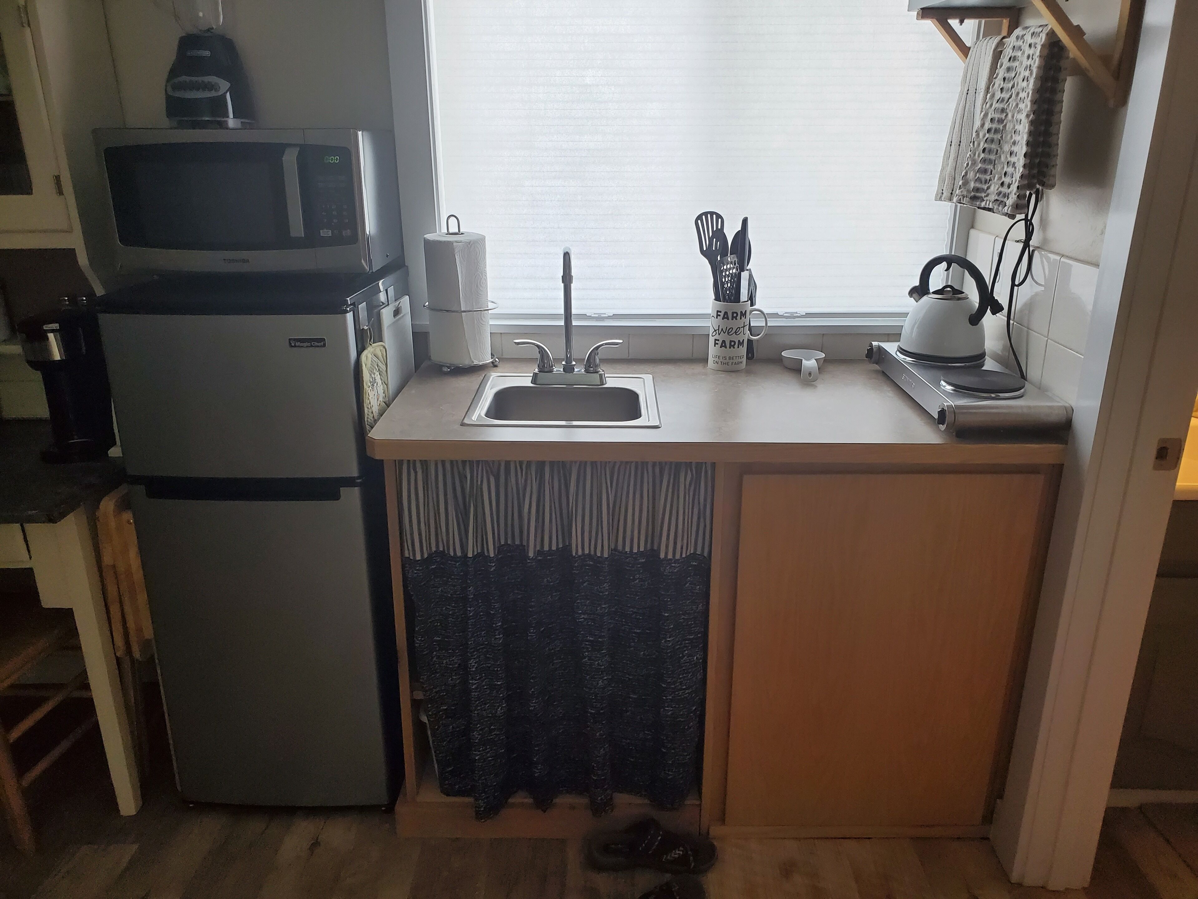 A compact kitchen with a refrigerator, microwave, sink, and a kettle on the countertop.