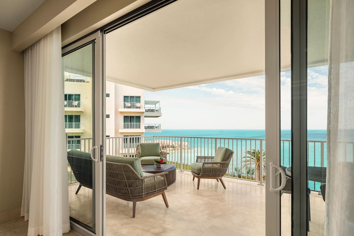 A balcony with wicker furniture, a glass door, and a view of the ocean.
