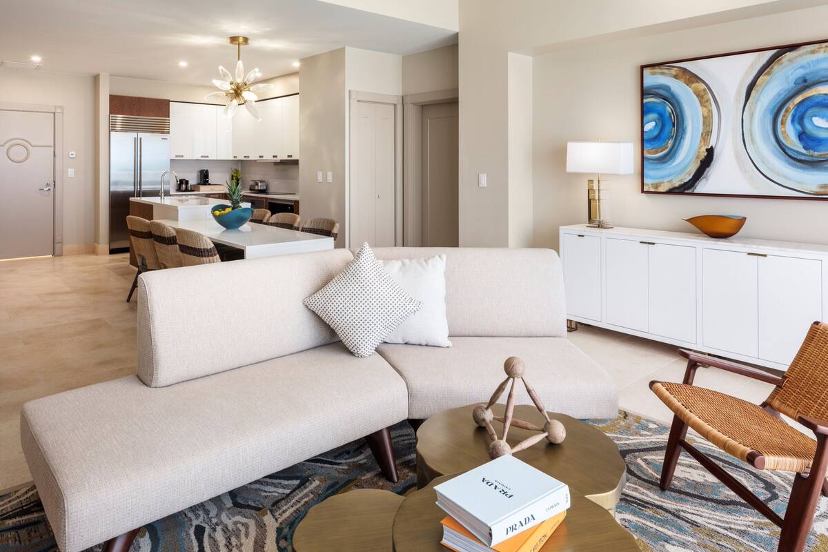 A modern living room with a sofa, coffee table, and a dining area in the background.