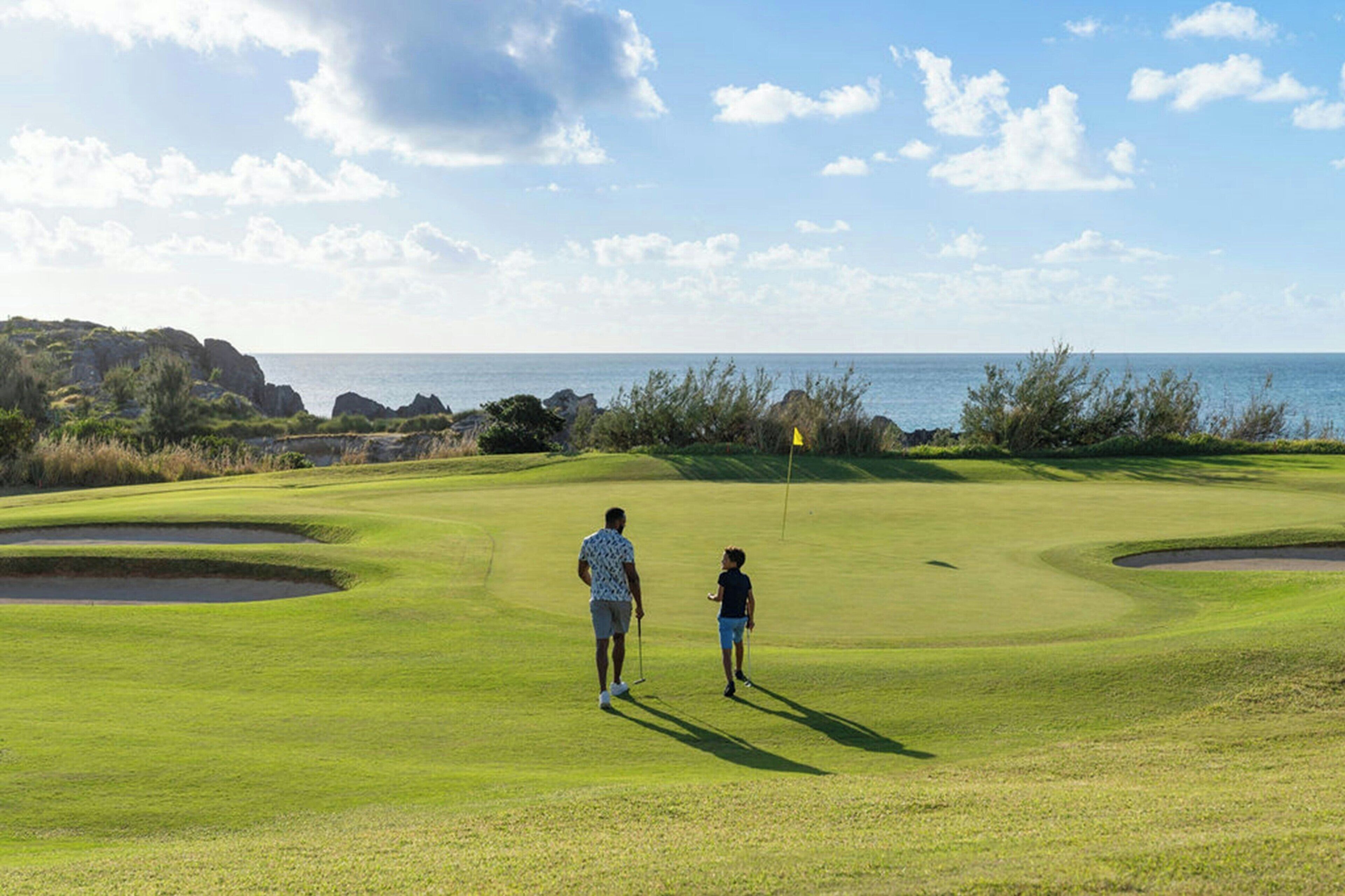 Un campo de golf con vista despejada al océano y terreno rocoso al fondo.