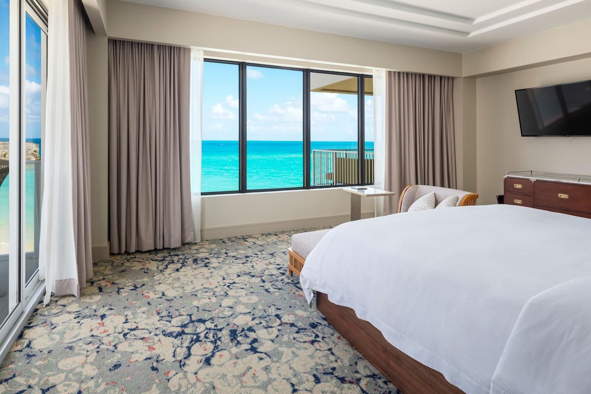 A hotel room with a large bed, a TV, and a view of the ocean.