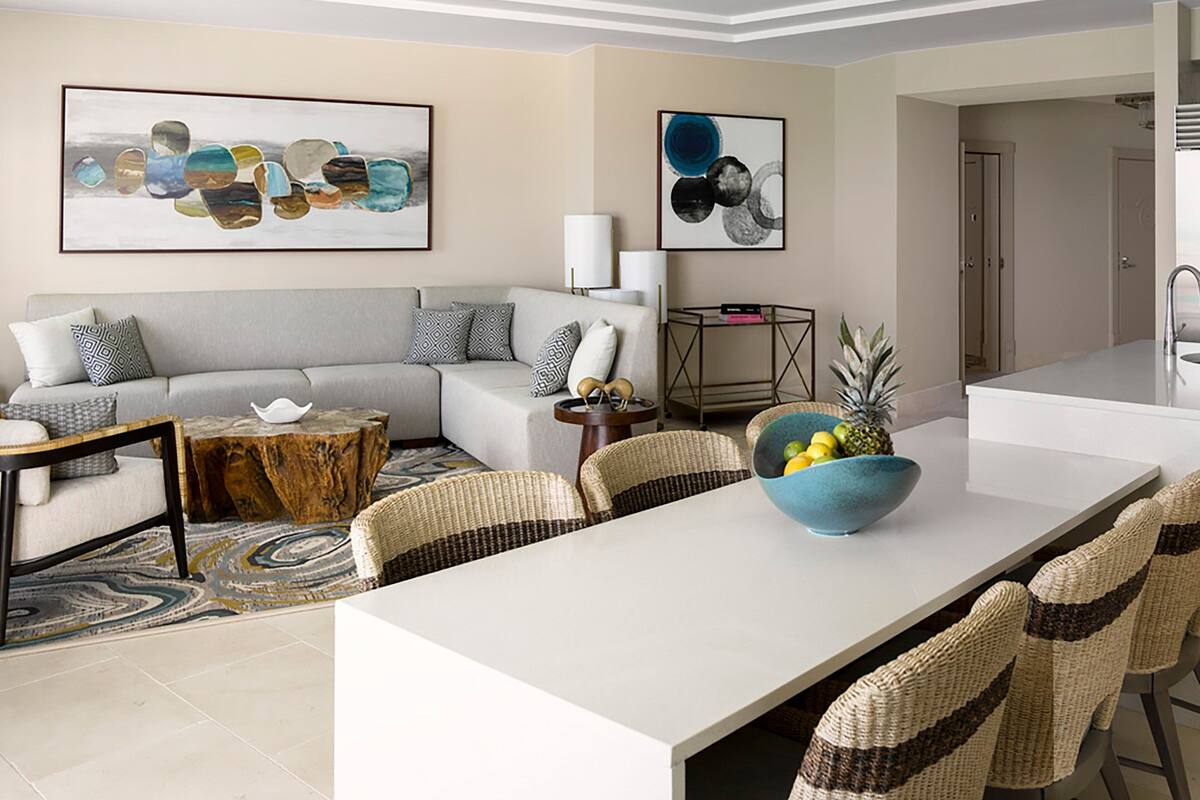 A modern living room with a sofa, dining table, and chairs. There are abstract paintings on the walls and a small side table with a lamp.