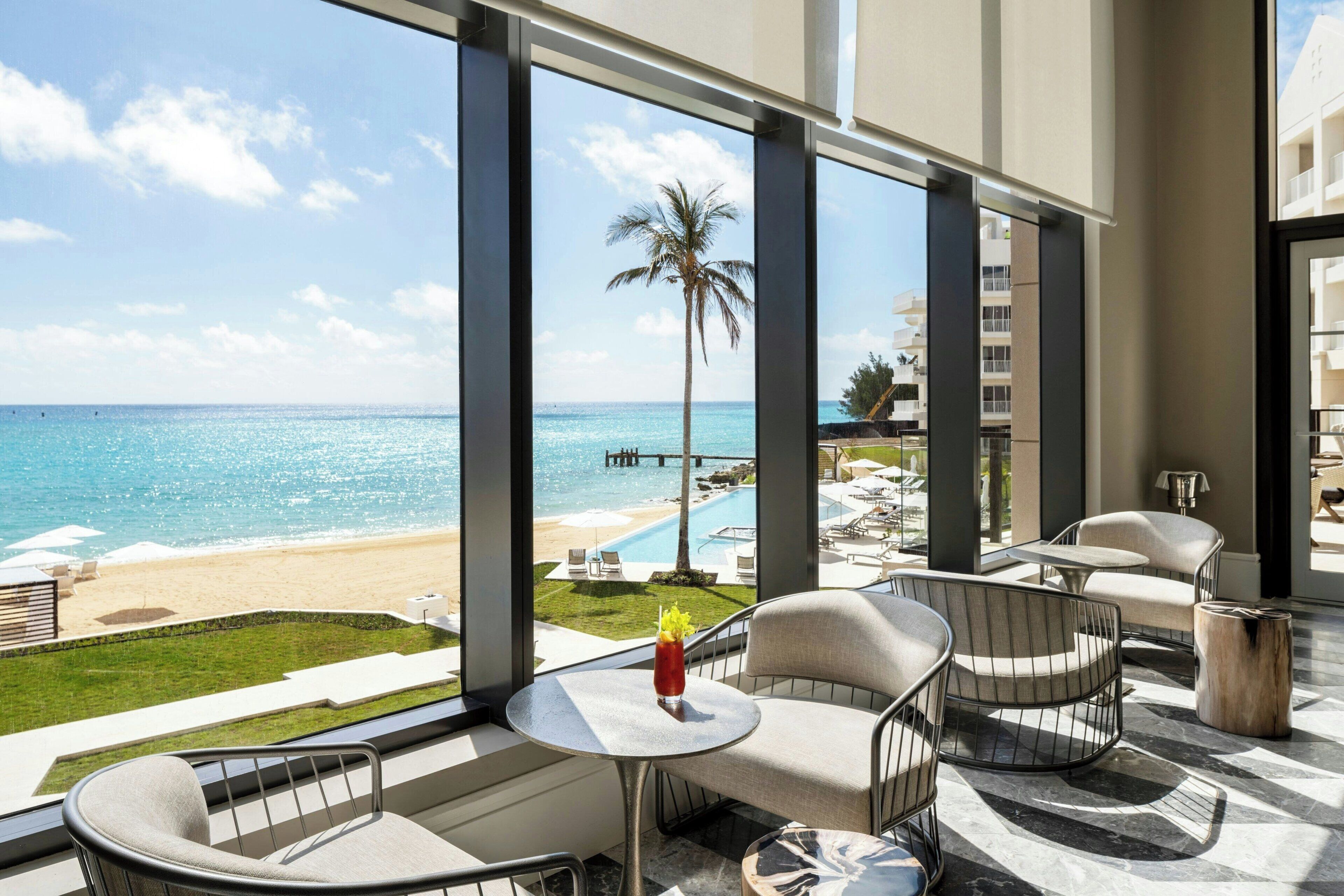 A balcony with a view of the beach and ocean, furnished with chairs and a table.