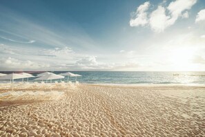 Una playa con sombrillas y sillas de playa blancas.