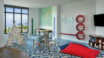 Un moderno salón infantil con un ventanal grande, una alfombra colorida y una estantería.