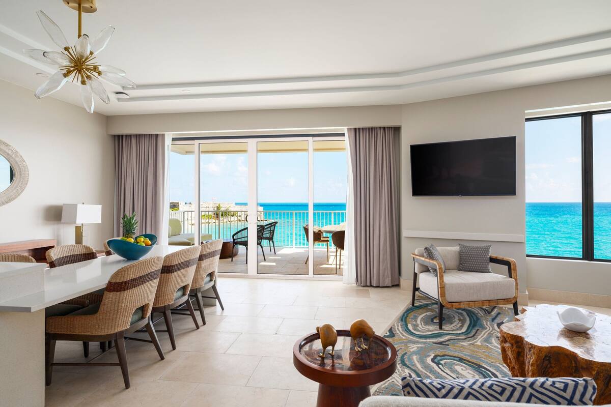 A hotel room with a balcony, dining area, and a TV.