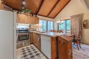 Una cocina con armarios de madera, horno de acero inoxidable y lavavajillas. Hay una alfombra a cuadros en el suelo y una mesa de comedor con sillas.