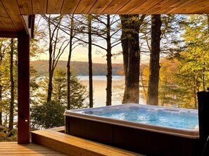 A hot tub on a wooden deck with a view of a lake and trees.