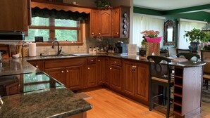 A kitchen with wooden cabinets, granite countertops, and a central island. - Chalet w/ Lake & MT views, Hot Tub, Pet friendly,  <10mins to Lake & Golf (Wells)