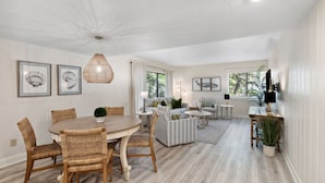 A spacious living area with a dining table, sofas, and a coffee table. There are framed pictures on the walls and a ceiling light fixture. - Pet Friendly | Ground Floor Beachwood Condo | Renovated Kitchen | Across the Street from the Beach (Fernandina Beach)