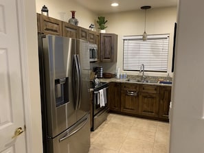 A kitchen with wooden cabinets, a stainless steel refrigerator, a microwave, and a sink.