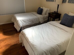 Una habitación con dos camas individuales, una mesita de noche con lámpara y una ventana con persianas.