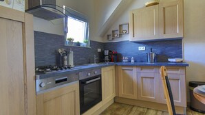 A modern kitchen with wooden cabinets, a built-in oven, a stove, and a coffee maker. - Gîte au pré des oies (Ostheim)