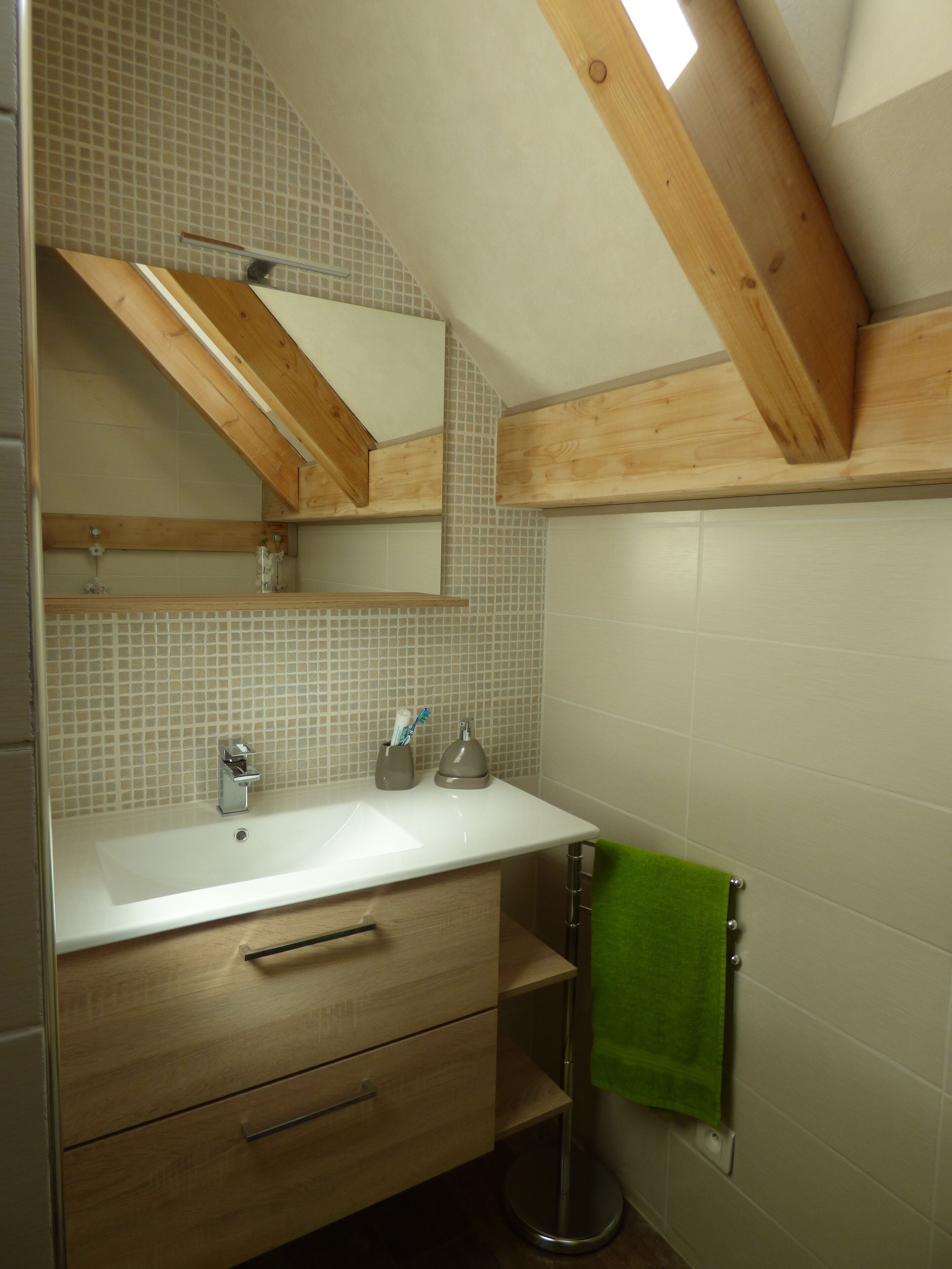 A bathroom with a white sink, wooden vanity, a green towel, and a mirror above the sink.