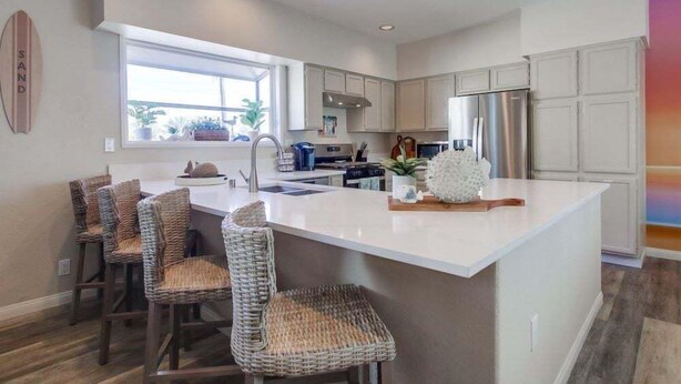 Una cocina moderna con una isla grande, muebles blancos y vistas al exterior.