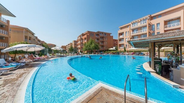 En swimmingpool omgivet af liggestole og parasoller, med et barområde på den ene side.