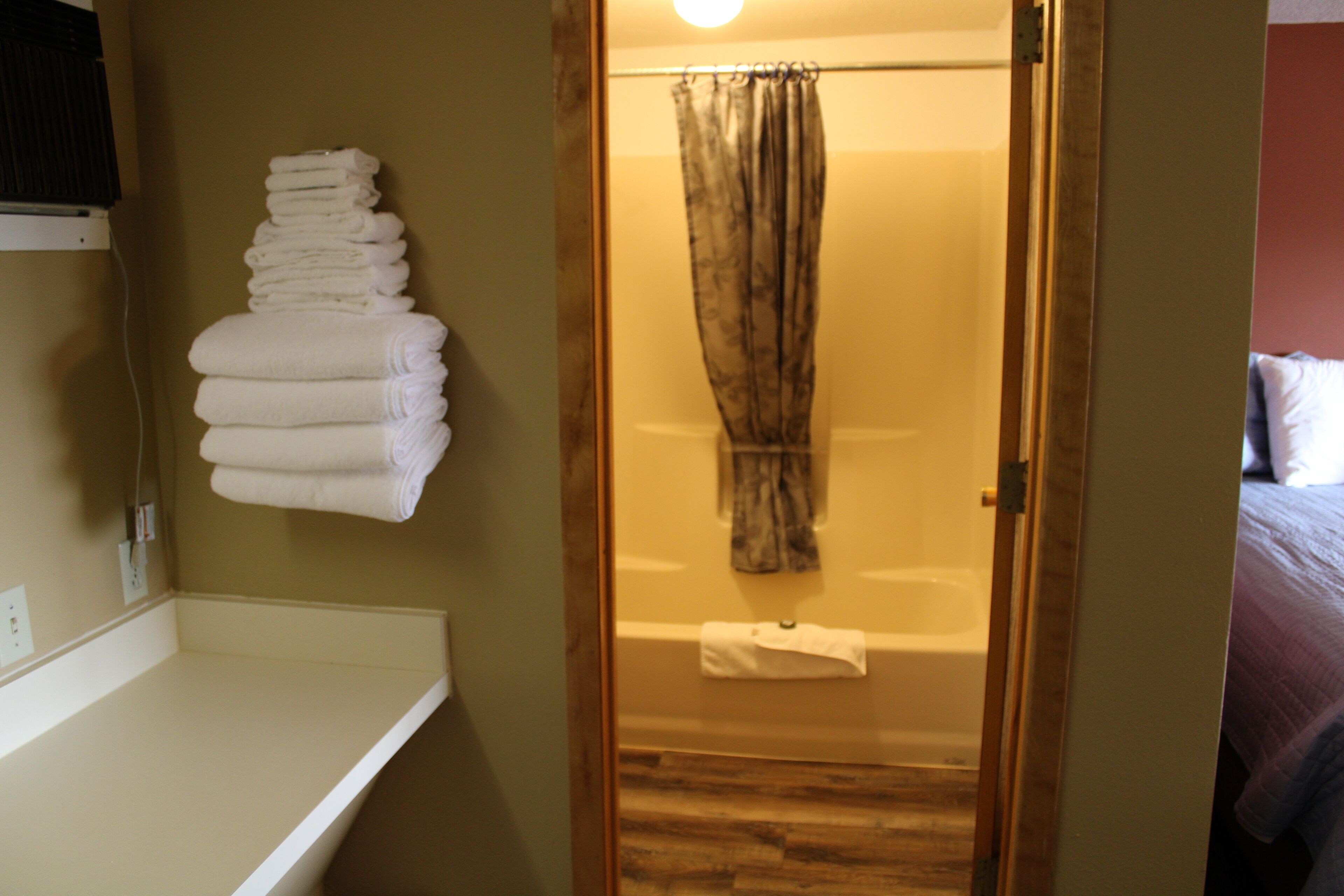 A bathroom with a wooden door, a white bathtub, and a towel rack with folded towels.