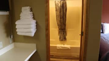 A bathroom with a wooden door, a white bathtub, and a towel rack with folded towels.