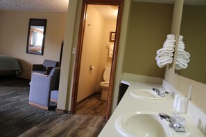 A hotel room with a wooden floor, a single bed, a chair, two sinks, and a mirror. - Adoba Dreamland (Gulliver)