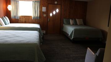 Une chambre avec deux lits, des murs en bois, un sol recouvert de moquette et une porte avec une pancarte.