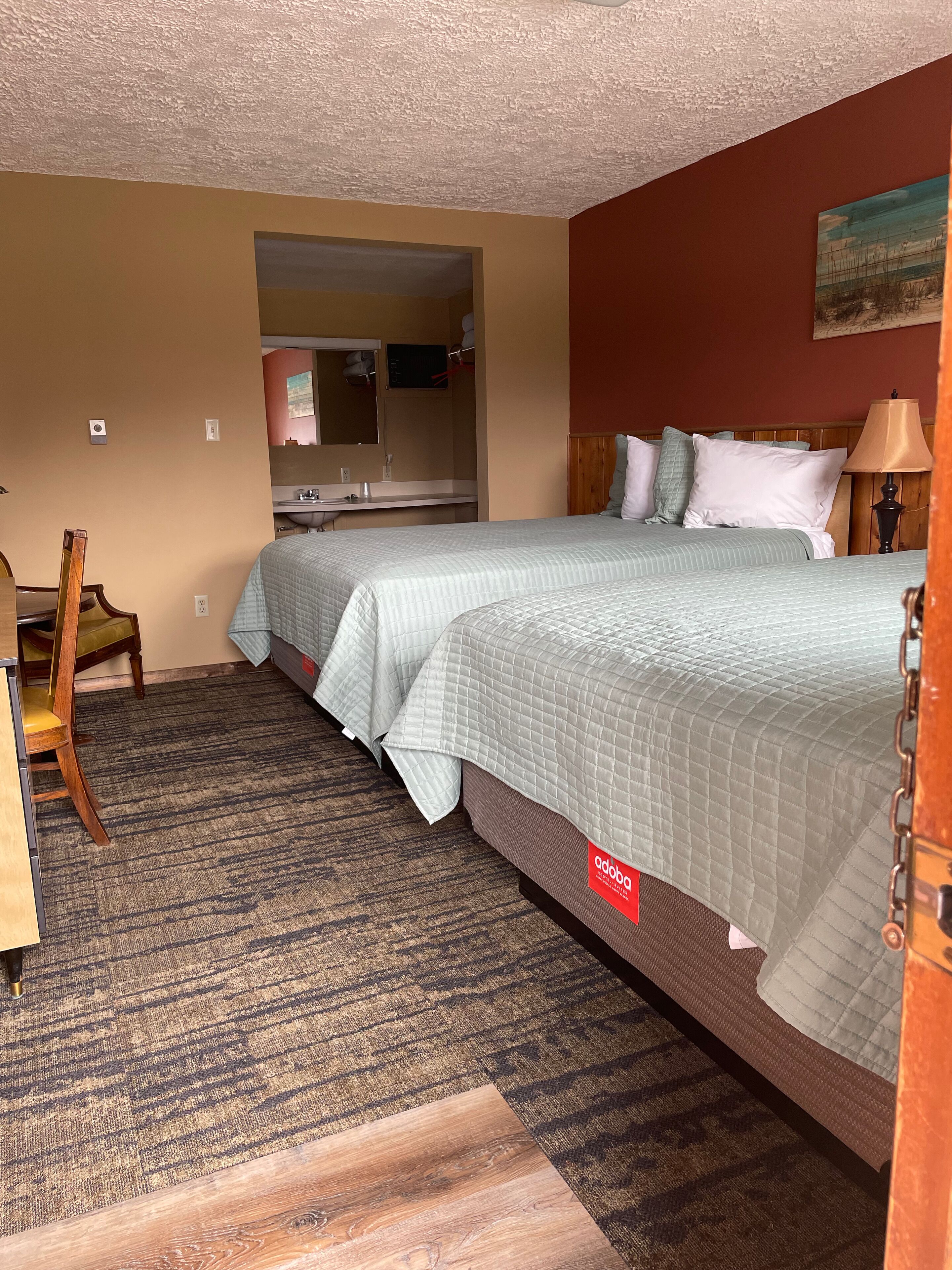 A hotel room with two beds, a desk, and a bathroom visible through an open door.
