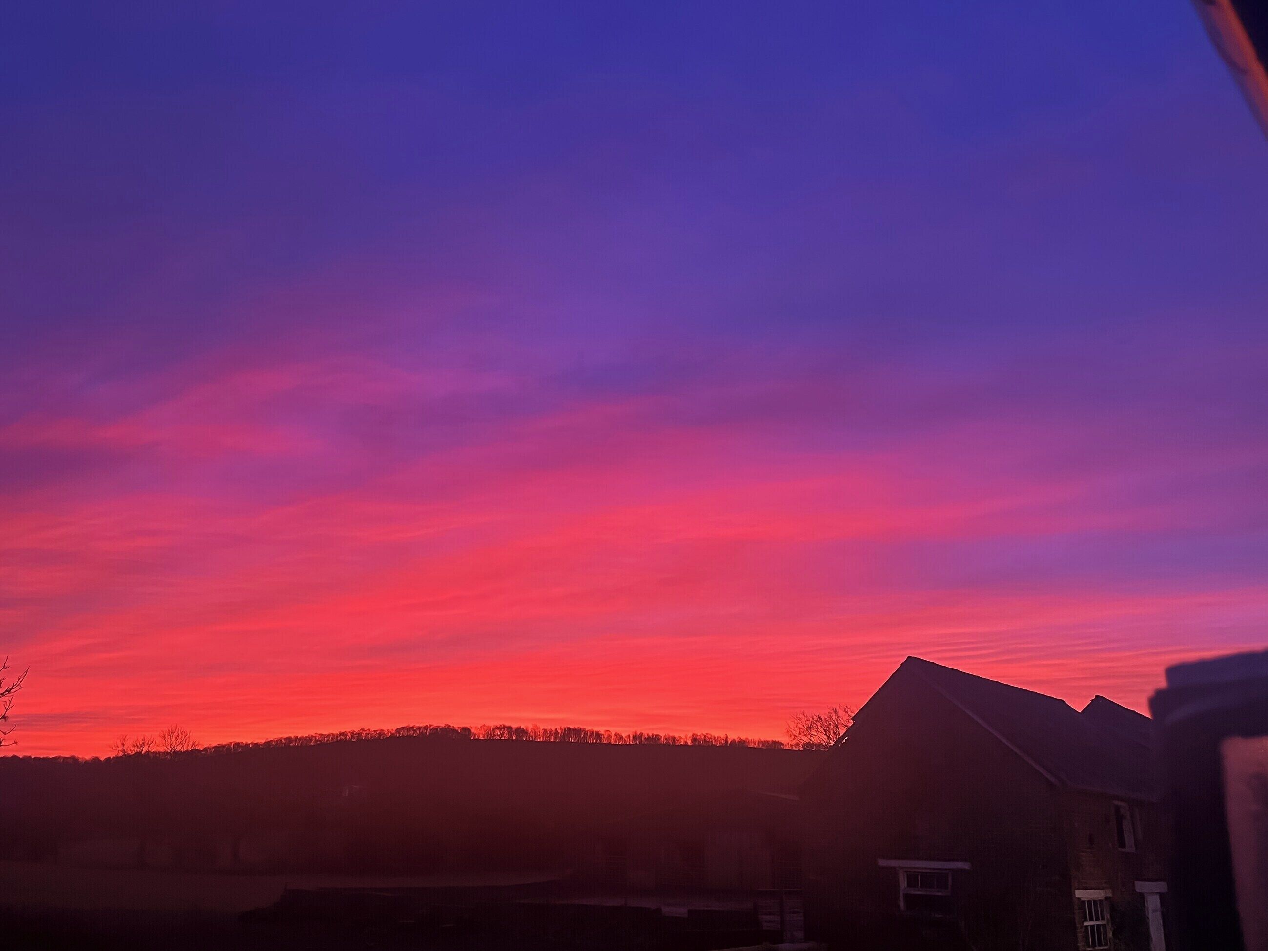 Ein Sonnenuntergang über einer Wohngegend mit Häusern und einer Erhebung im Hintergrund.