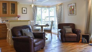 A living room with a brown leather sofa, a dining table with chairs, and a bay window with curtains.