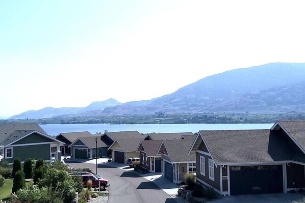 A residential area with houses, a driveway, and a lake with mountains in the background.