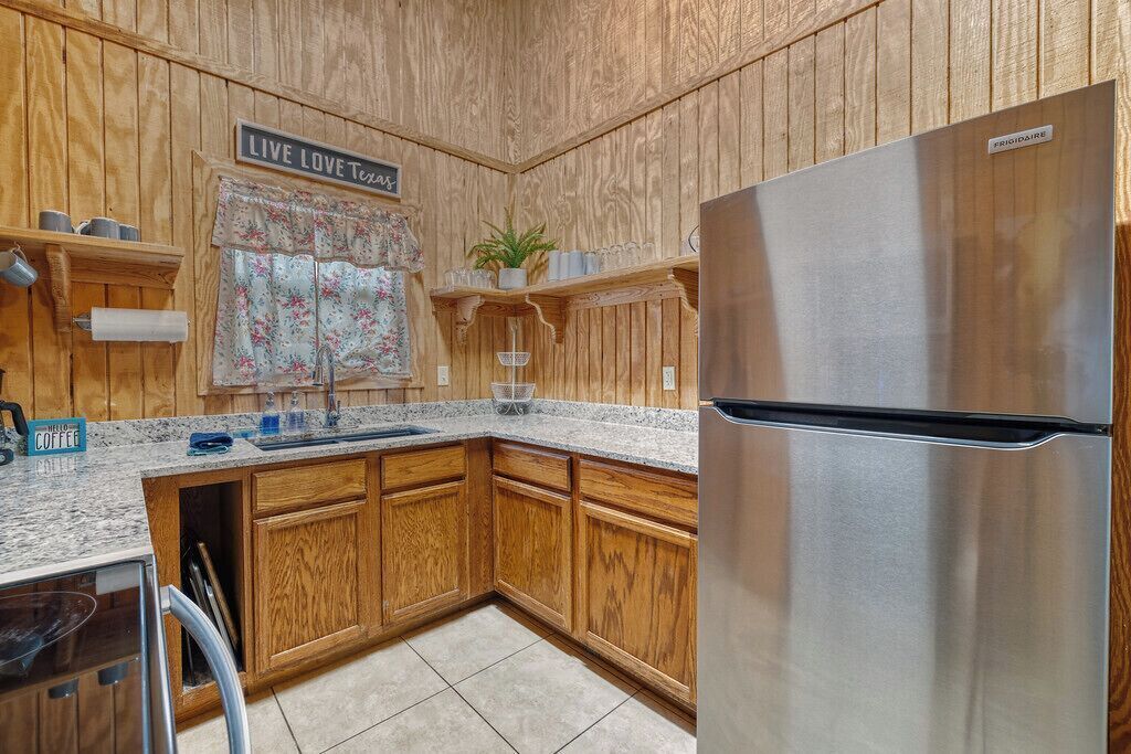 A kitchen with wooden cabinets, a stainless steel refrigerator, and a granite countertop.