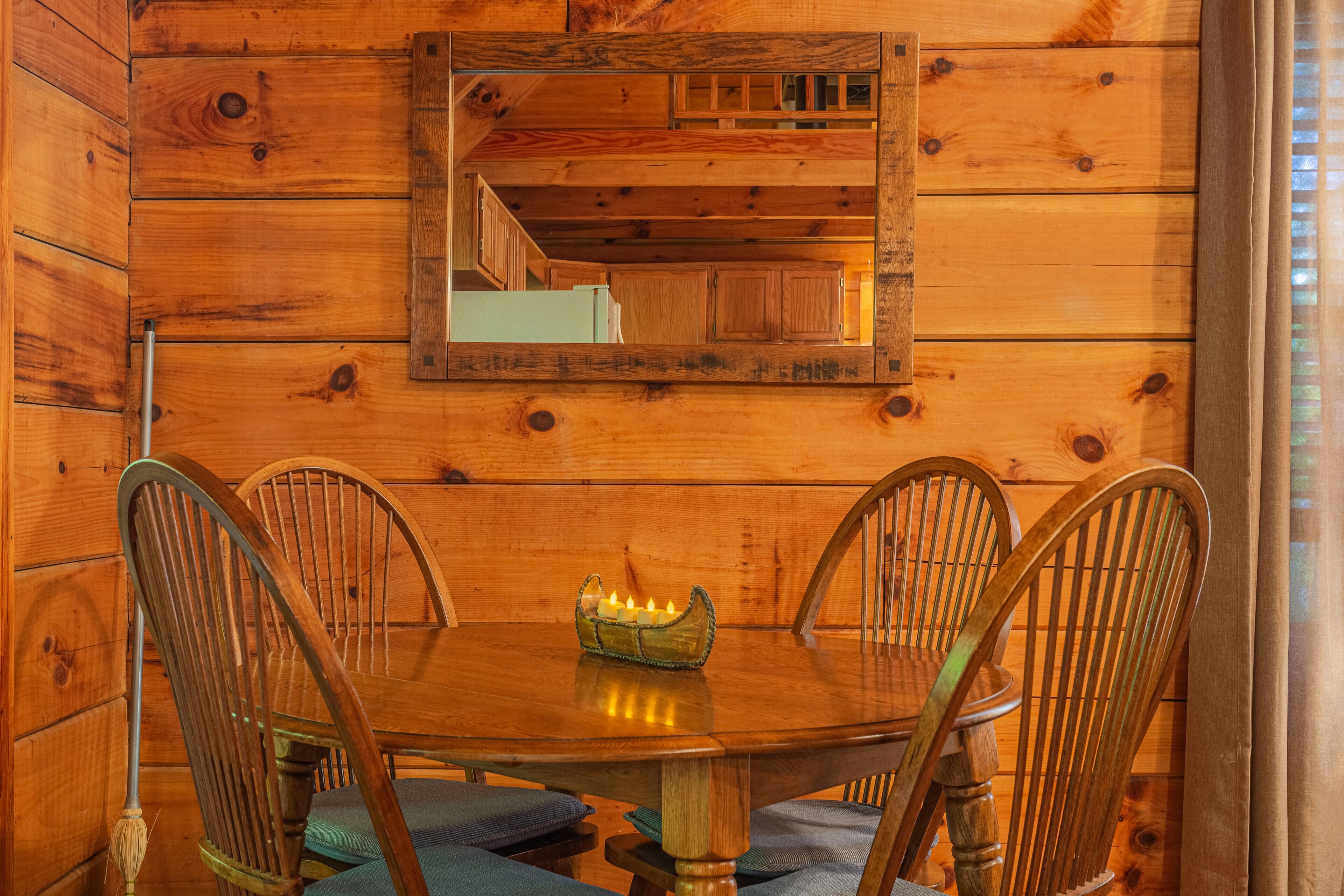 A wooden dining room with a round table, four chairs, and a mirror on the wall.