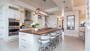 Una cocina moderna con una isla central, taburetes de bar, electrodomésticos de acero inoxidable y una lámpara colgante.
