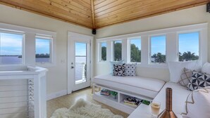 Una habitación moderna y luminosa con techo de madera, ventanas amplias, un sofá blanco y una mesita de centro blanca.