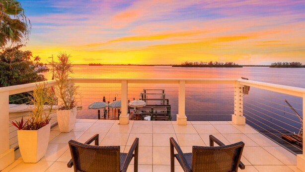 Terraza con sillas y mesas con vistas a un cuerpo de agua al atardecer.