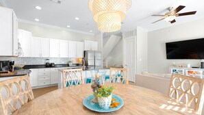Une cuisine moderne avec des meubles blancs, un coin repas doté d’une table en bois et un ventilateur de plafond.
