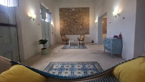 Een gang met een getextureerd vloerkleed, een houten schommelstoel, een klein tafeltje en een blauwe ladekast.