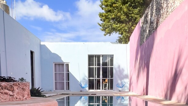Een modern zwembadgedeelte met helder water, een wit gebouw en een roze muur.