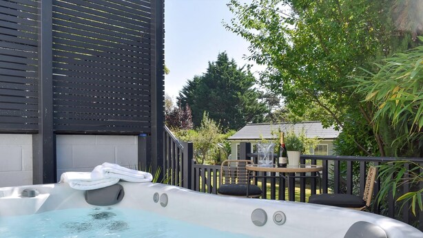 A hot tub with a wooden deck, a table with chairs, and a house in the background. - The White House Retreat (Worthing)