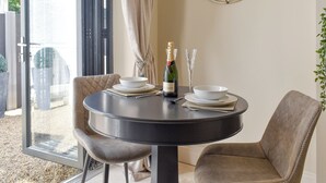 A round dining table with two chairs, a bottle of champagne, and a glass on the table. - The White House Retreat (Worthing)