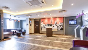 A hotel lobby with a reception desk, seating area, and a digital information kiosk. - Premier Inn Newquay - Seafront (Newquay)