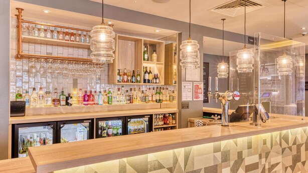 Eine Bar mit Regalen voller Flaschen, einer Kühlvitrine und hängenden Leuchten.